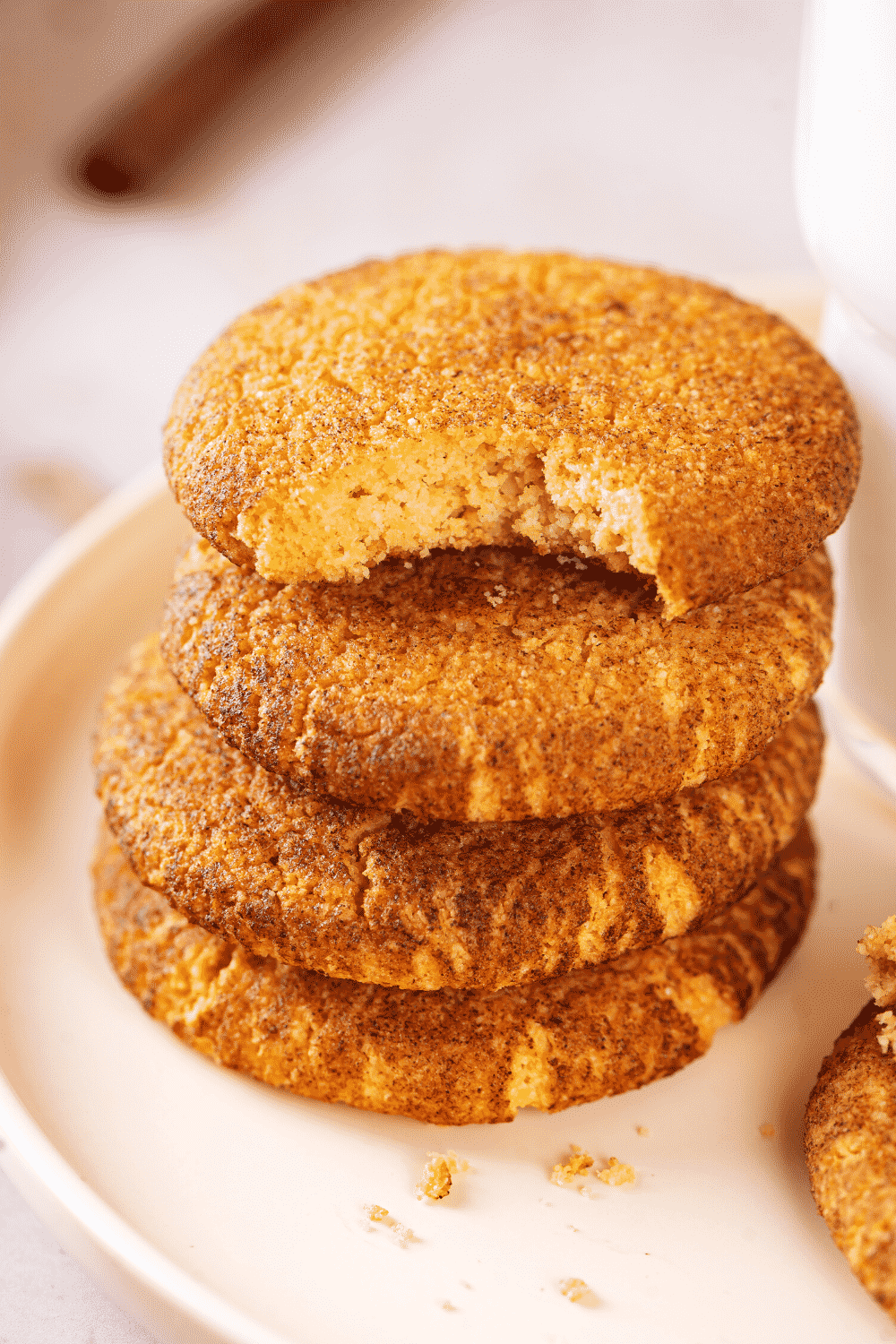 A stack of four snickerdoodle cookies on a white plate. The top cookie has a bite out of the front of it.