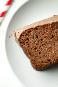 A slice of chocolate yogurt cake topped with frosting on a white plate.