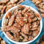 A white bowl filled with candied pecans. The bowl is set on a blue napkin.