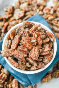 A white bowl filled with candied pecans. The bowl is set on a blue napkin.