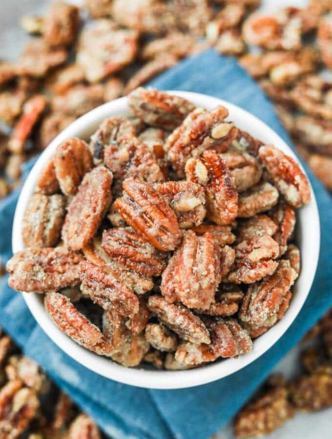 A white bowl filled with candied pecans. The bowl is set on a blue napkin.