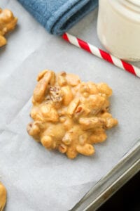 A peanut butter nut cluster on a baking sheet lined with white parts from paper and placed next to a red and white paper straw.
