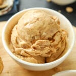 A white bowl filled with peanut butter ice cream. The bowl is on a wooden cutting board.