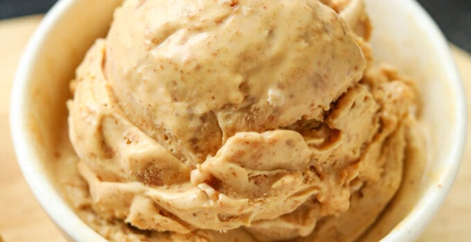 A white bowl filled with peanut butter ice cream. The bowl is on a wooden cutting board.