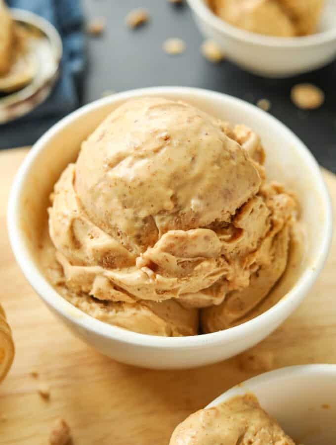 A white bowl filled with peanut butter ice cream. The bowl is on a wooden cutting board.