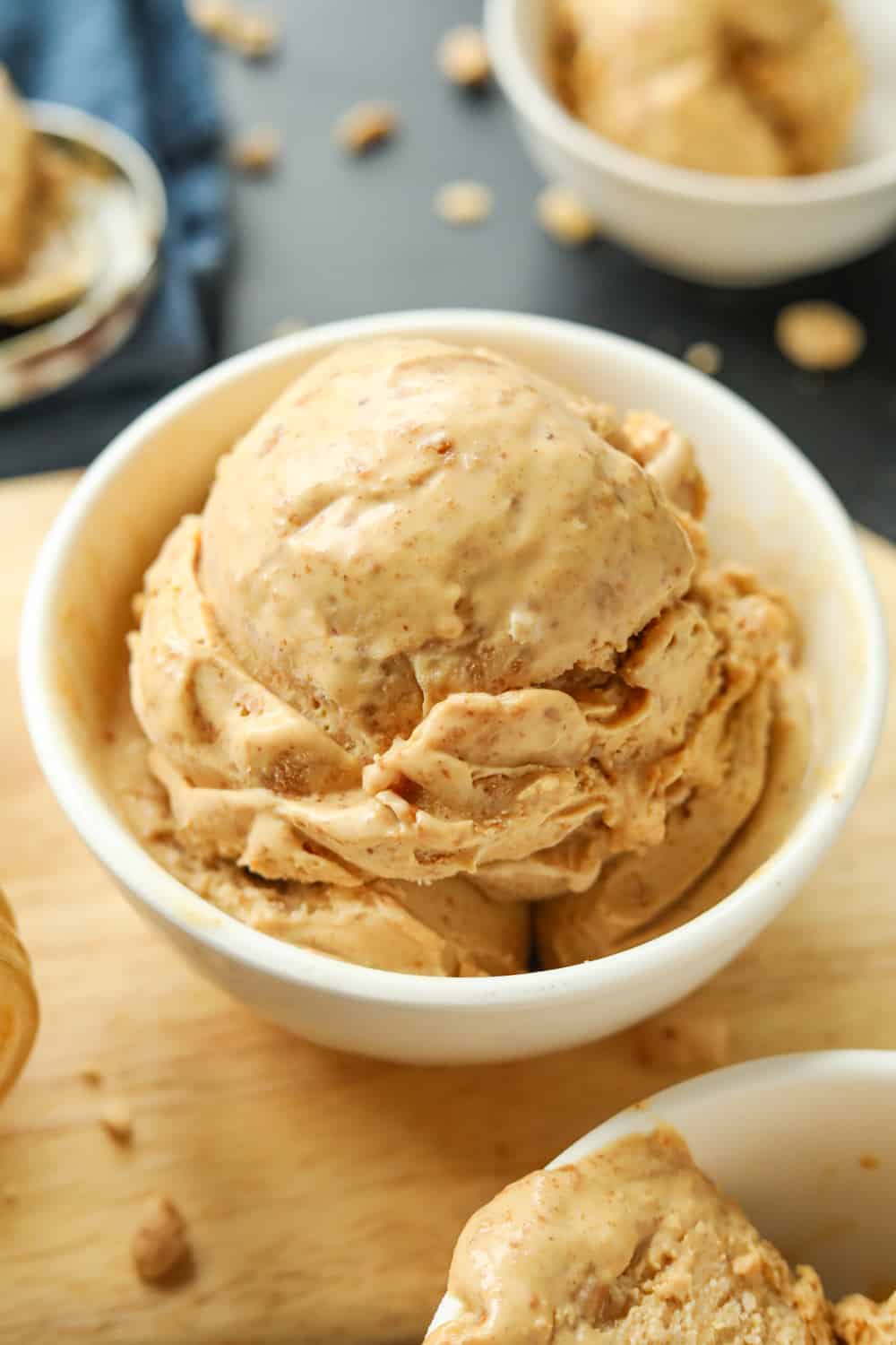A white bowl filled with peanut butter ice cream. The bowl is on a wooden cutting board.