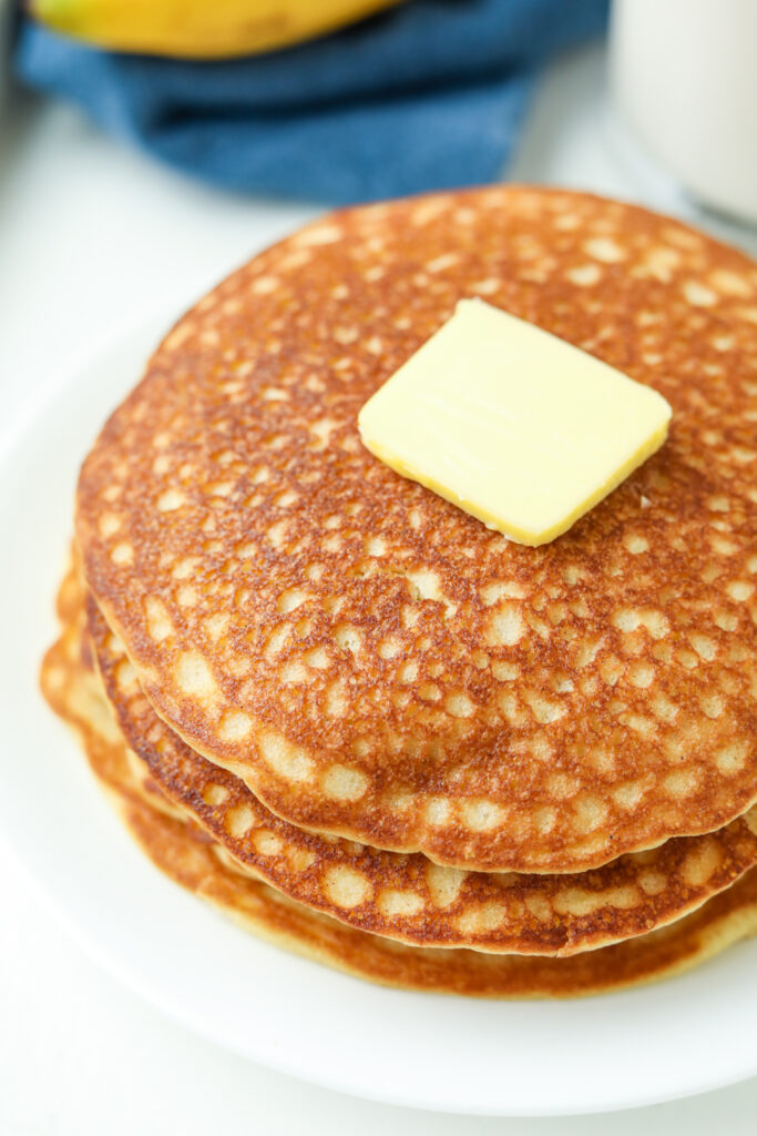 A stack of banana pancakes topped with butter on a white plate.