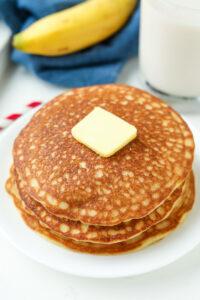 A stack of pancakes on a white plate topped with butter.