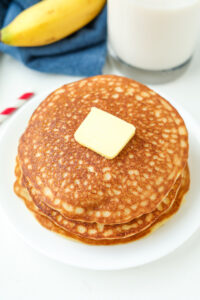 A stack of pancakes topped with butter. The pancakes are on a white plate.