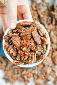 A hand holding a white bowl filled with candied pecans.