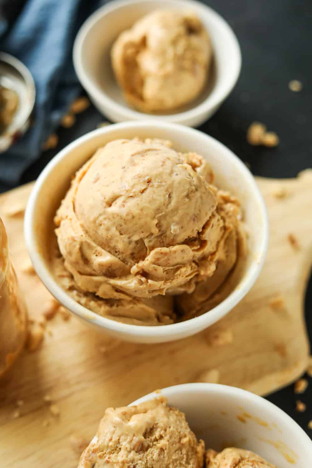 A white bowl filled with peanut butter ice cream on a wooden cutting board with other white bowls filled with ice cream around it.