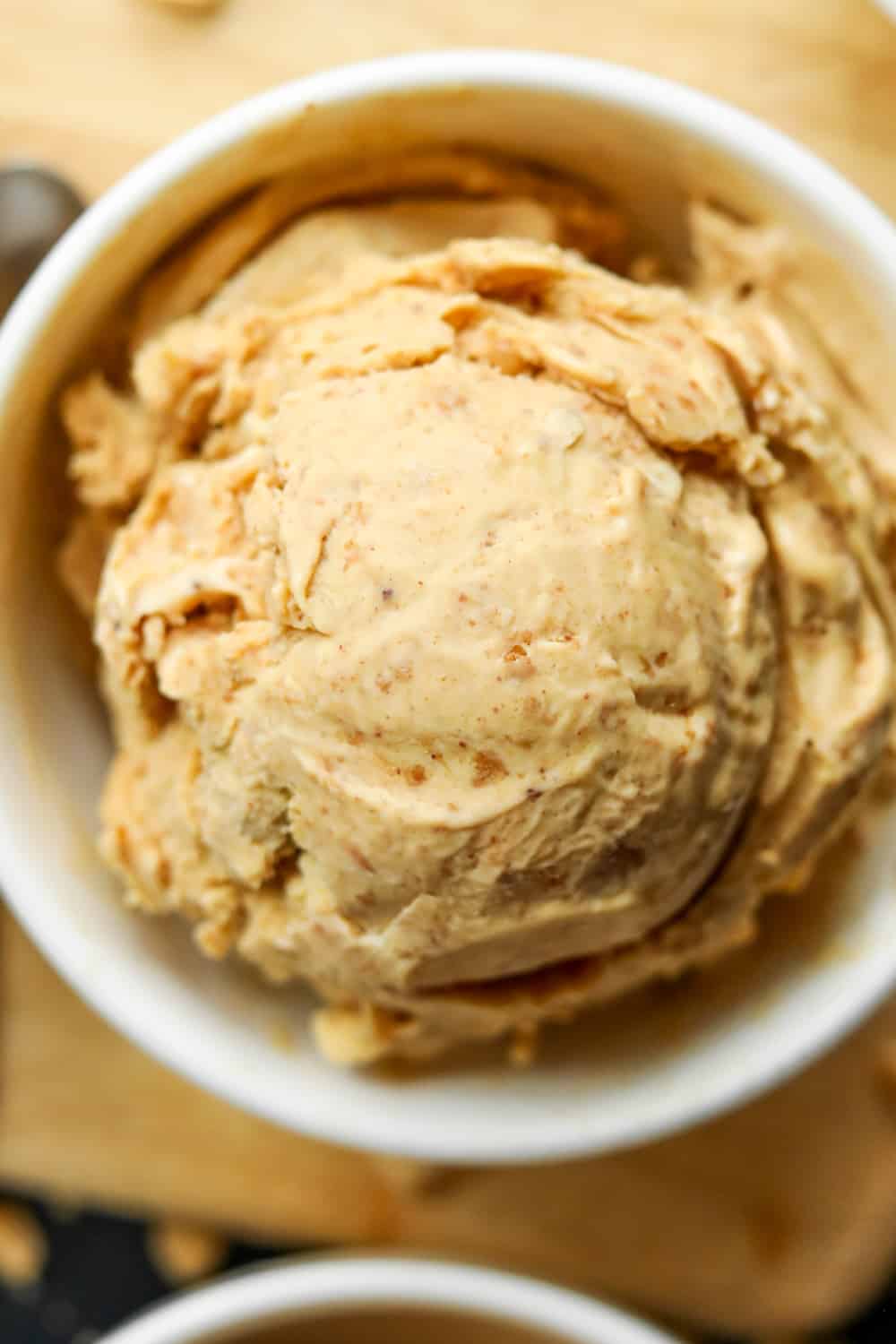 A white bowl filled with peanut butter ice cream on a wooden cutting board.