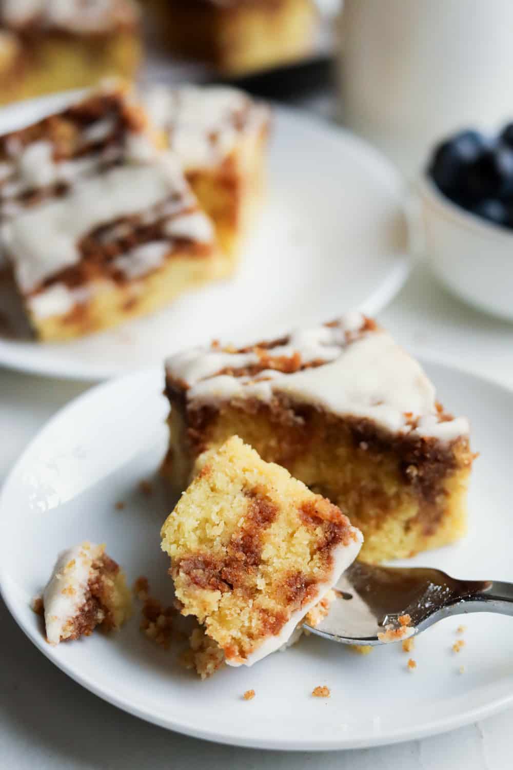 A piece of coffee cake on a white plate with a fork holding a piece of the cake.