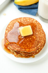 A stack of pancakes with covered in butter and maple syrup.