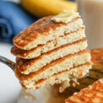 A fork pulling out a bunch cut up pancakes from a stack of them.