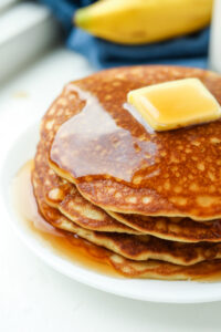 The side of a stack of pancakes with maple syrup running off of them.