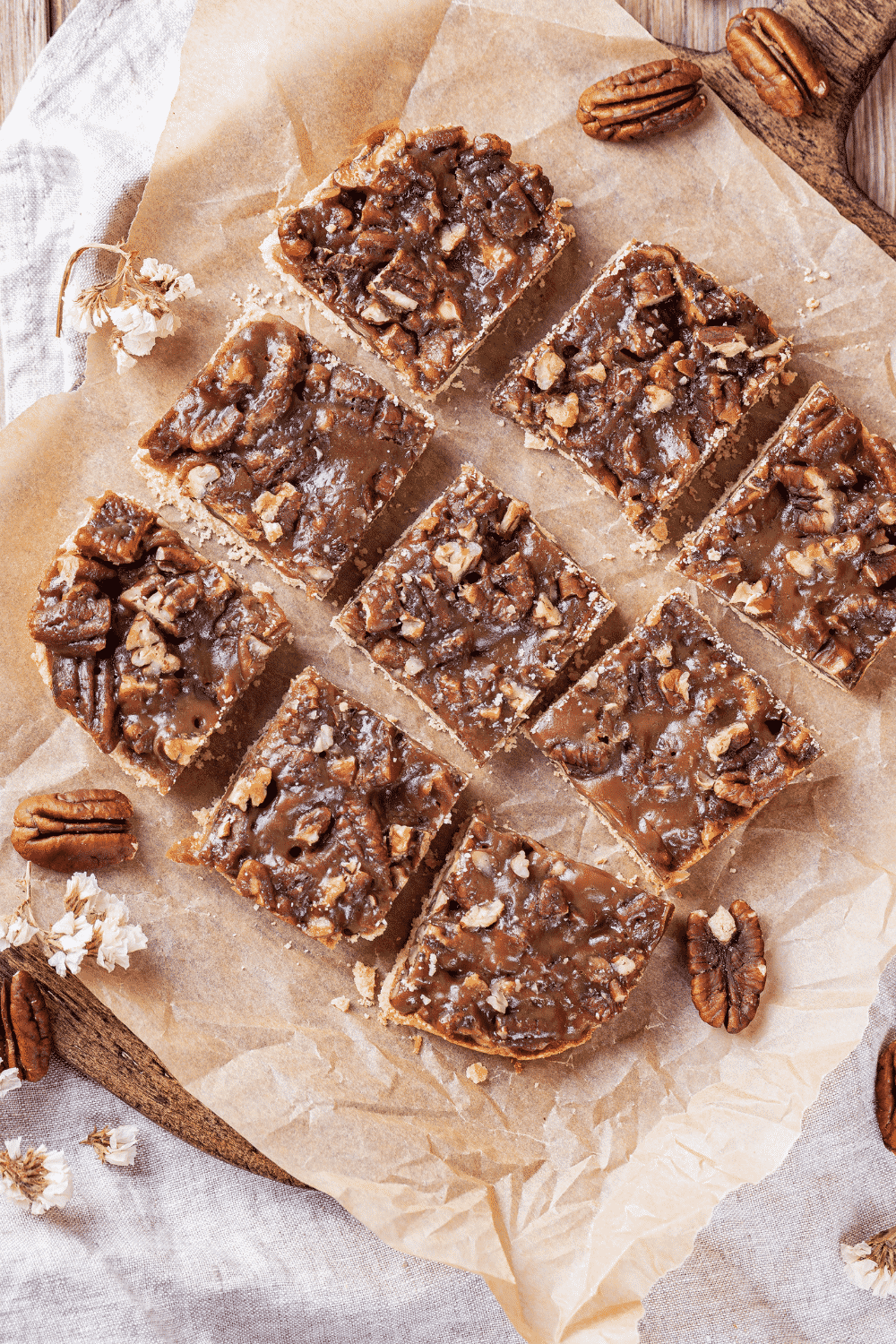 Three rows of three pecan pie bars on a piece of parchment paper on a wooden cutting board.