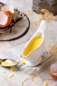 Gravy bowl filled with hollandaise sauce. The gravy boat is on a piece of newspaper on a white counter.