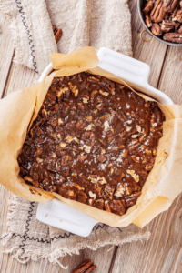 A baking dish lined with parchment paper with pecan pie bar filling on top.