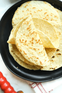 Two folded tortilla shells on top of a few other tortilla shells on a black plate.