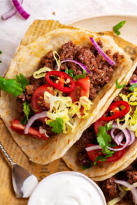 A ground beef taco and half of a ground beef taco and a piece of newspaper on a plate.