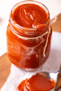 A glass jar filled to the top with barbecue sauce. Some barbecue sauce is dripping over the front edge of the jar.