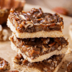 Three pecan pie bars stacked on top of each other on a piece of parchment paper.