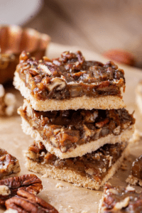 Three pecan pie bars stacked on top of each other on a piece of parchment paper.