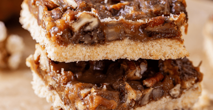 Three pecan pie bars stacked on top of each other on a piece of parchment paper.