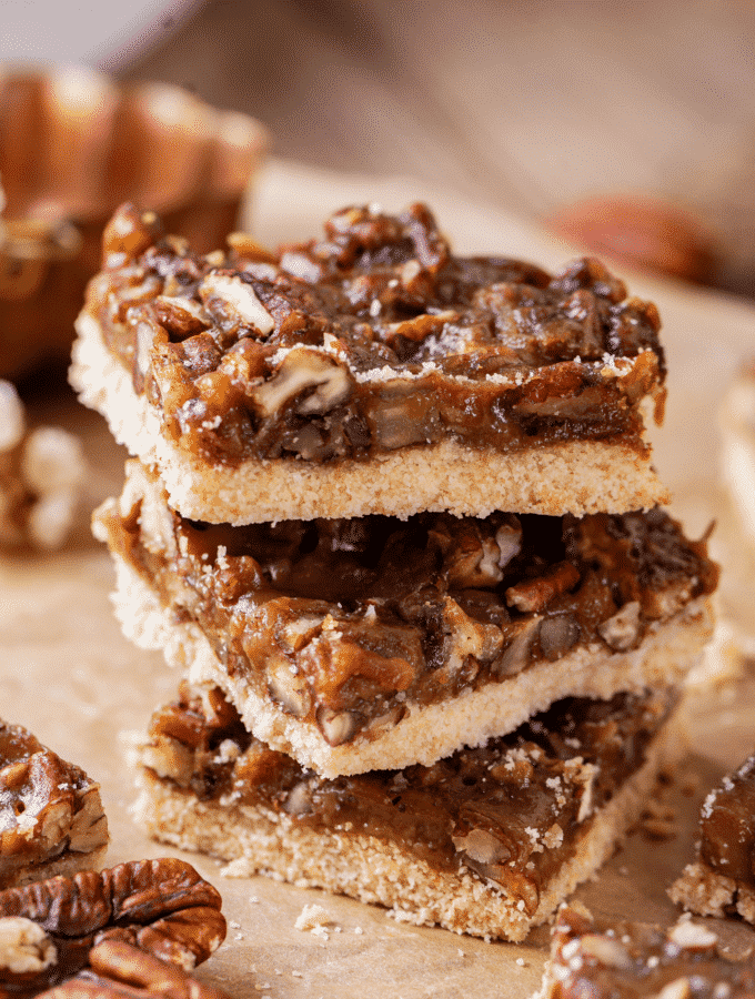 Three pecan pie bars stacked on top of each other on a piece of parchment paper.