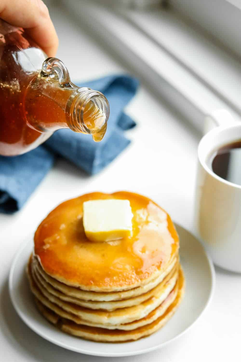 Maple syrup just about to be poured on a stack of pancakes.