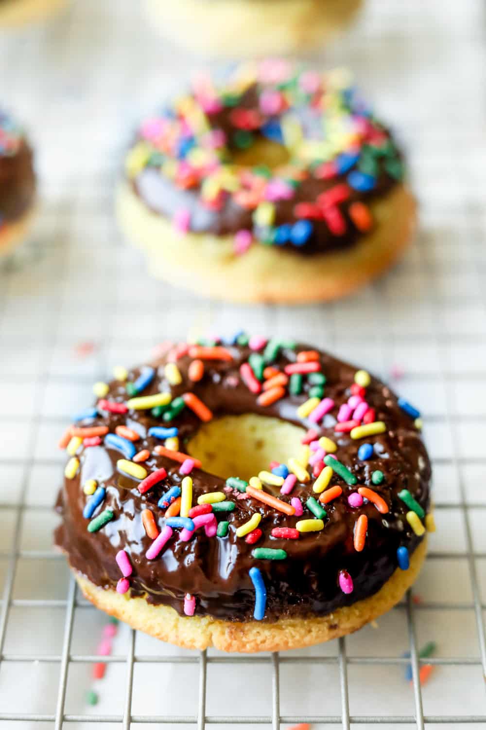 Vanilla donuts that I've been dipped in chocolate and covered in multicolored sprinkles on the silverware rack.