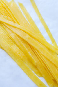 Keto pasta strands laid on top of white parchment paper. The pasta strands are stacked on top of one another.