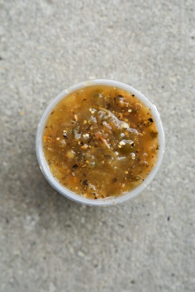 A cup of salsa on a cement floor.