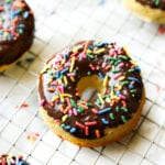 A chocolate covered donut on a wire rack. The donut is topped with sprinkles.