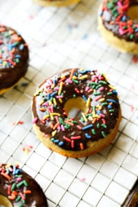 A chocolate covered donut on a wire rack. The donut is topped with sprinkles.