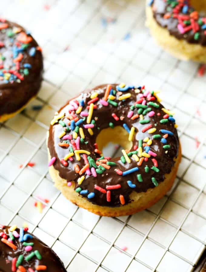 A chocolate covered donut on a wire rack. The donut is topped with sprinkles.