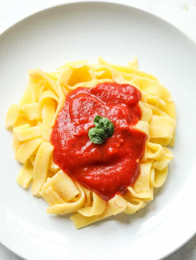 A plate of linguini pasta that's been topped with red sauce.