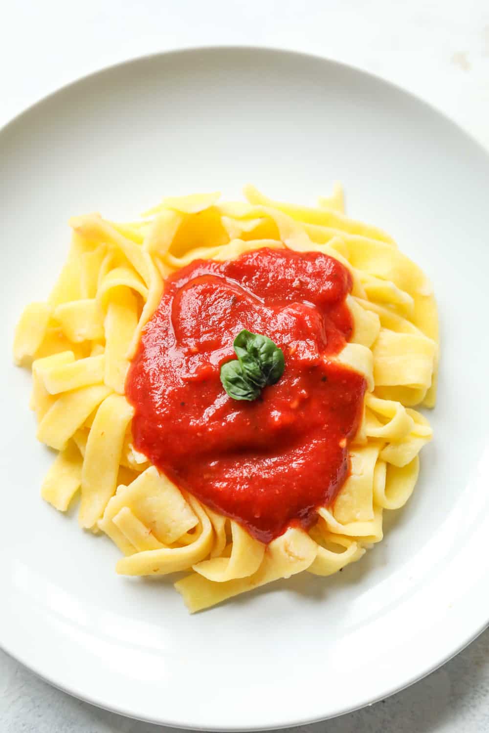 A plate of linguini pasta that's been topped with red sauce.