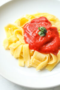 Noodles on a white plate. The noodles are covered in tomato sauce.