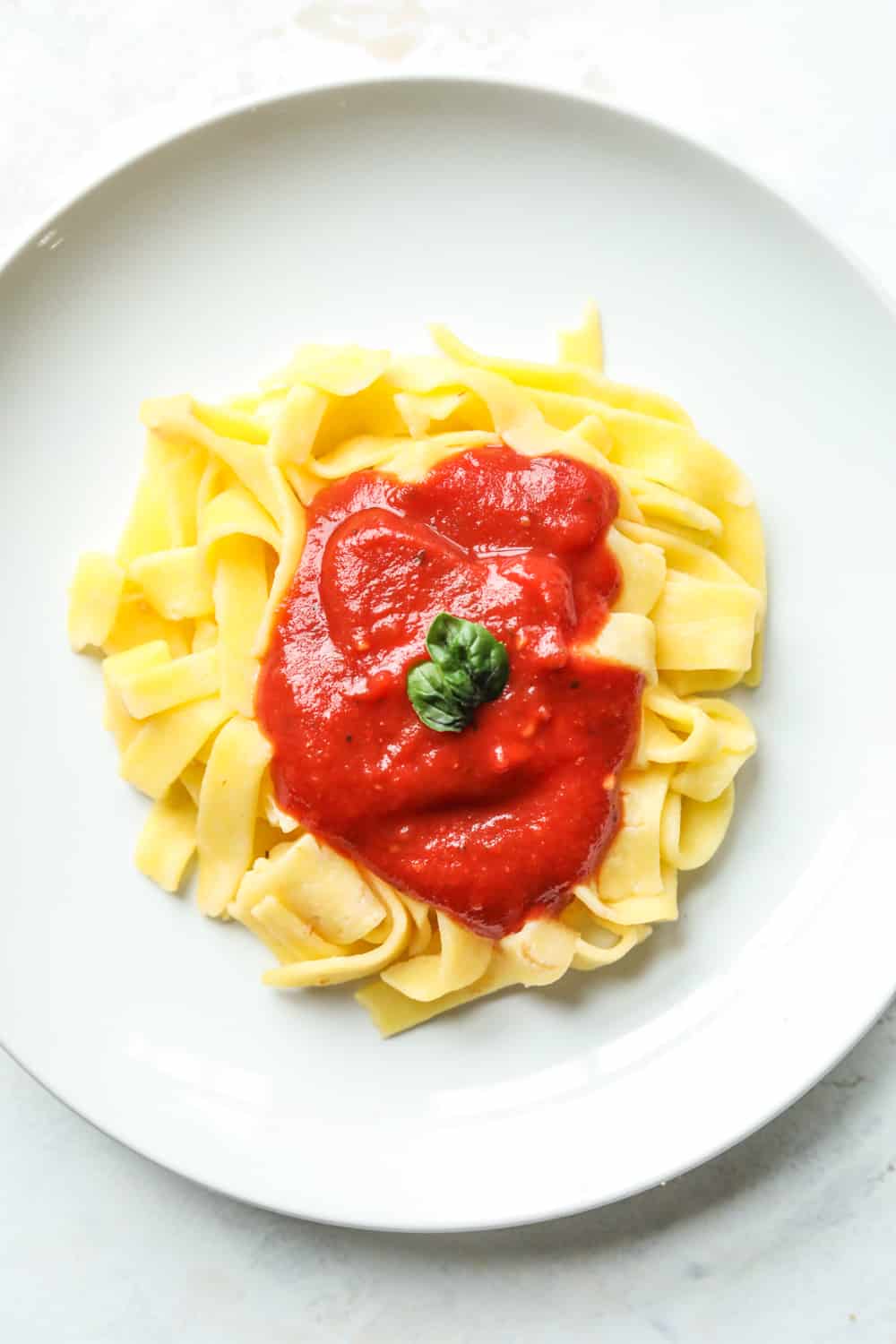 Pasta on a plate, covered in tomato sauce, and topped with basil.