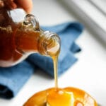 Maple syrup being poured over a stack of pancakes.