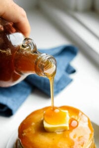 Maple syrup being poured over a stack of pancakes.