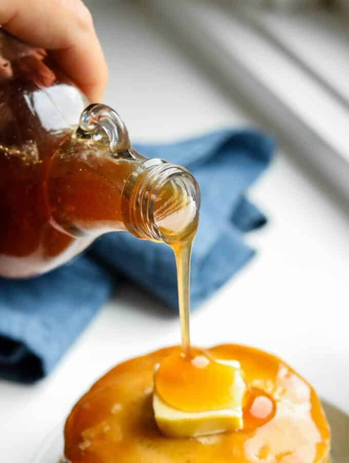 Maple syrup being poured over a stack of pancakes.