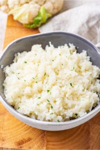 A gray bowl filled with cauliflower rice on a wooden cutting board.