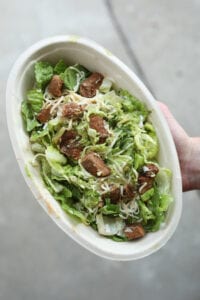 A hand holding a keto chipotle salad bowl with yes, steak, shredded cheese, and guacamole.