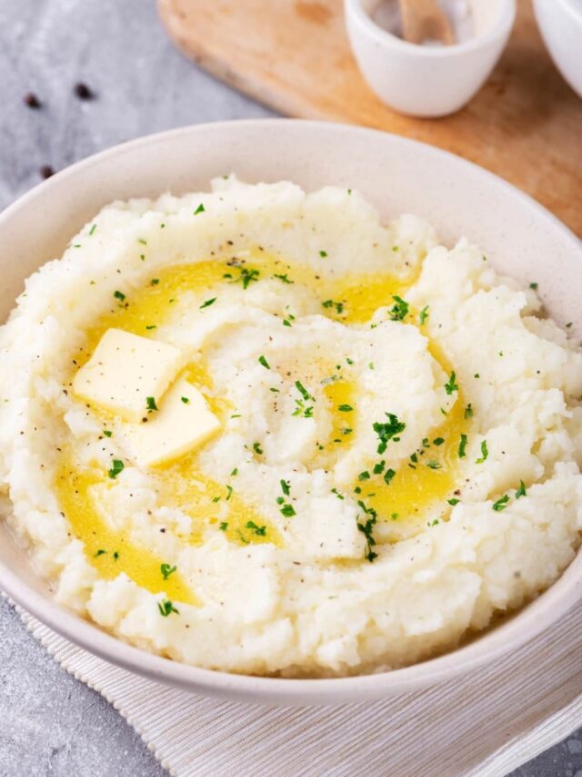 Hawaii bowl filled with cauliflower mashed potatoes. The ball is on a white tablecloth on a gray counter and there is part of a wooden cutting board behind it.