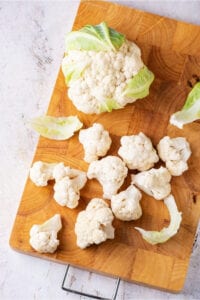 Board with a head of cauliflower and a few cauliflower florets on it.