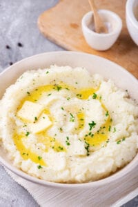 Hawaii bowl filled with cauliflower mashed potatoes. The ball is on a white tablecloth on a gray counter and there is part of a wooden cutting board behind it.