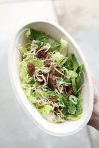 A hand holding a keto chipotle salad bowl with steak, lettuce, and shredded cheese.